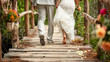 Barefoot bride and groom walk on a rustic bridge adorned with flower petals and floral arrangements.