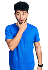 Canvas Print - Young arab man with beard wearing casual blue t shirt looking fascinated with disbelief, surprise and amazed expression with hands on chin