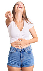 Wall Mural - Young beautiful blonde woman wearing casual white tshirt laughing at you, pointing finger to the camera with hand over body, shame expression