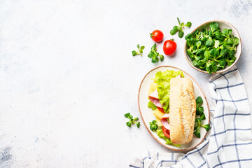 Canvas Print - Ciabatta sandwich with lettuce, cheese, tomatoes and ham. Flat lay on white table.