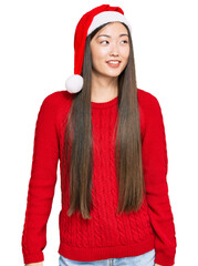 Wall Mural - Young chinese woman wearing christmas hat looking away to side with smile on face, natural expression. laughing confident.