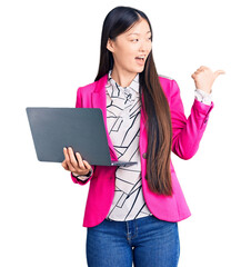 Sticker - Young beautiful chinese woman using laptop pointing thumb up to the side smiling happy with open mouth