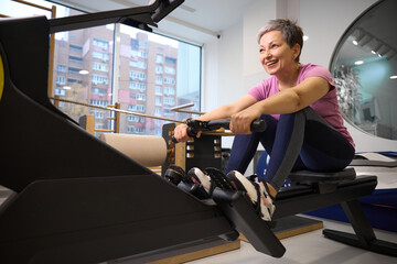 Adult smiling caucasian woman doing sport exercise for back on rowing trainer