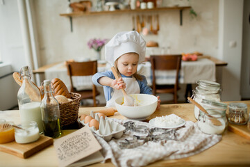 Girl cook 3 years old in a beautiful kitchen, in a chef's hat, in an apron, daylight