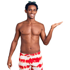 Wall Mural - African handsome man wearing swimsuit and sunglasses smiling cheerful presenting and pointing with palm of hand looking at the camera.