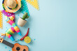 Top view shot of Cinco de Mayo decorations: hat, a vihuela, cactus in a pot, a colorful pinata, flag garlands, chilli peppers, confetti, placed on a pastel blue scene, space for text