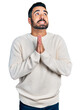 Young hispanic man with beard wearing casual white sweater begging and praying with hands together with hope expression on face very emotional and worried. begging.