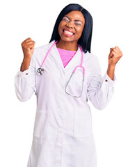 Wall Mural - Young african american woman wearing doctor stethoscope very happy and excited doing winner gesture with arms raised, smiling and screaming for success. celebration concept.