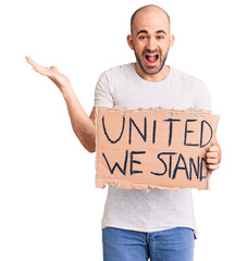 Canvas Print - Young handsome man holding united we stand banner celebrating victory with happy smile and winner expression with raised hands