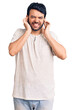 © Krakenimages.com - Young hispanic man wearing casual clothes covering ears with fingers with annoyed expression for the noise of loud music. deaf concept.