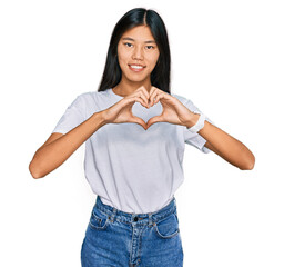 Poster - Beautiful young asian woman wearing casual white t shirt smiling in love doing heart symbol shape with hands. romantic concept.