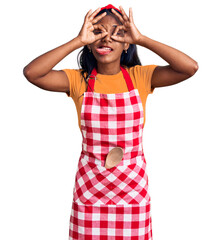 Wall Mural - Young indian girl wearing professional baker apron doing ok gesture like binoculars sticking tongue out, eyes looking through fingers. crazy expression.