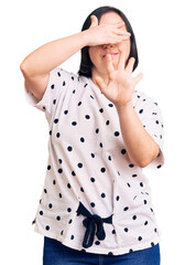 Poster - Brunette woman with down syndrome wearing casual clothes covering eyes with hands and doing stop gesture with sad and fear expression. embarrassed and negative concept.