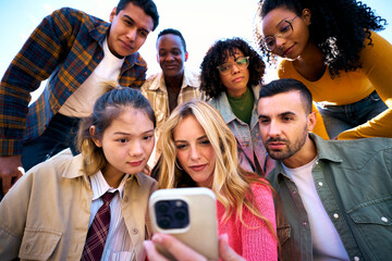 A group of serious human face using mobile smiling watching something on a digital display. Technology addicted Friends looking at cell phone. They are sharing a joyful moment through gestures.
