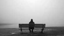 A Lonely Man Sitting On A Bench By The Lake In A Foggy Day