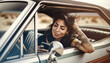 Road Trip themed scene with an Ethnic Latina woman checking her smartphone in a parked classic muscle car out in the desert