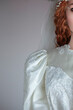 Bride with red hair wearing a vintage wedding dress against a lain backdrop. The dress was photogrpahed on a mannequin and the face and neck were added using AI 