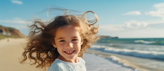 Wall Mural - A young girl stands on the beach with her hair blowing in the wind, smiling at the sky. She looks happy and content, enjoying the leisure of the landscape and the sound of the water