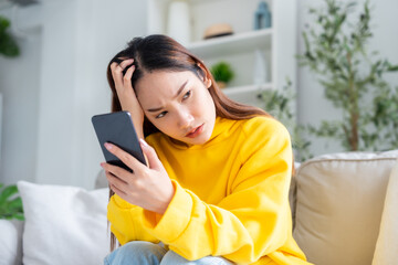 Bad news on device screen. Upset asian woman frustrated by problem with work or relationships, sitting on couch, feeling despair and anxiety, loneliness, having psychological trouble