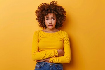 Wall Mural - a worried woman in a yellow shirt touching her stomach on yellow studio background