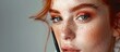 A woman with red hair and freckles is enhancing her features by applying makeup with a brush, focusing on her nose, lips, eyes, and jawline, creating a stunning makeover