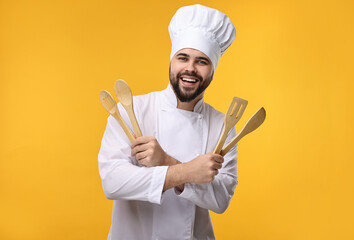 Sticker - Happy young chef in uniform holding wooden utensils on orange background