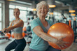 Two women are working out in a gym, one of them holding a large orange ball. Scene is energetic and positive, as the women are smiling and seem to be enjoying their workout