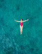 Aerial View of a Woman in Red Swimsuit Floating Serenely on the Crystal Clear Ocean Waters During Midday