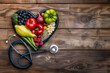 Top view of a heart-shaped arrangement of healthy foods with stethoscope on a wooden background.