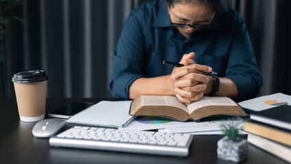 Woman with hands clasped praying while sitting at desk in office. Businesswoman praying at work. Contemplative prayer thinking in office. Hands folded in prayer gesture beg about something.