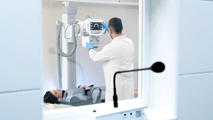 Sticker - A specialist doctor in an X-ray room, a radiologist sets up a machine for radiography of a patient and makes a scan. The concept of medical technologies, modern medical equipment.