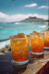 Three glasses of orange juice with ice cubes and straws. The glasses are on a table by the ocean