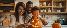 An Ethnically Diverse Family With A Smiling Son Creates Jack O Lanterns From Pumpkins While Celebrating Halloween In The Kitchen.