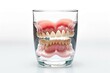 Denture inside glass of water. Teeth hygiene, care, prevention Isolated on white background