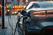 Electric car (EV) at charging station with the power cable supply plugged on blurred bokeh street light background.
