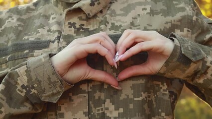 Wall Mural - Female servicewoman brave soldier dressed in the camouflage military uniform showing heart shape sign symbol of independence. Armed Forces of Ukraine. Woman serving in ukrainian army troops
