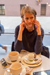 Woman in a coffee place on a phonecall with cups of coffee and tea on the table