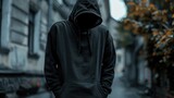 Fototapeta Zachód słońca - A man wearing a black hoodie standing on a city street. Suitable for urban themes