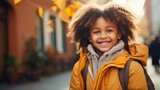 Fototapeta  - Portrait of a smiling young girl with curly hair wearing a yellow jacket and a backpack