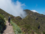 Fototapeta  - Man hiker in hat walking at paved footpath, hiking trail PR1.2 from Achada do Teixeira to Pico Ruivo mountain, the highest peak in the Madeira, Portugal.