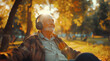 Grey hair and beard retired elderly man sitting on autumnal park bench, listening to wireless headphones and cheerful smiling. Happiness of senior retirement, success people and music lovers concept.