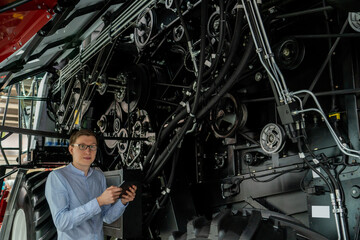 Poster - Serviceman with digital tablet on a next to ombine harvester with open hood..