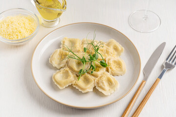 Poster - Traditional italian Ravioli stuffed pasta filled with mozzarella cheese decorated with green fresh pea microgreens served on plate with tableware, olive oil and glass of wine on white wooden table