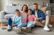 © Prostock-studio - Smiling family with preteen kids sitting on floor in cozy living room