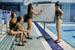 Young female athlete in swimwear moving small round magnets along whiteboard during presentation and discussion of training points