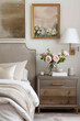 A light grey bedside table with two drawers, brass hardware and gold trim is placed next to the bed in front of an elegant headboard, soft lighting from wall sconces illuminates a vintage painting on 
