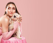 © Dimid - A young beautiful girl in a pink dress with a white small dog on a pink background.