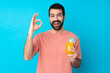 Young man over holding a cocktail over isolated blue background surprised and showing ok sign