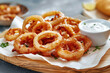 Close up of pile of fried crispy onion rings with white sauce on cutting board on grey concrete background. Tasty appetizer for beer