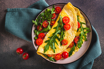 Wall Mural - Close up of french omelette filled with cherry tomatoes and arugula on a plate on the table top view